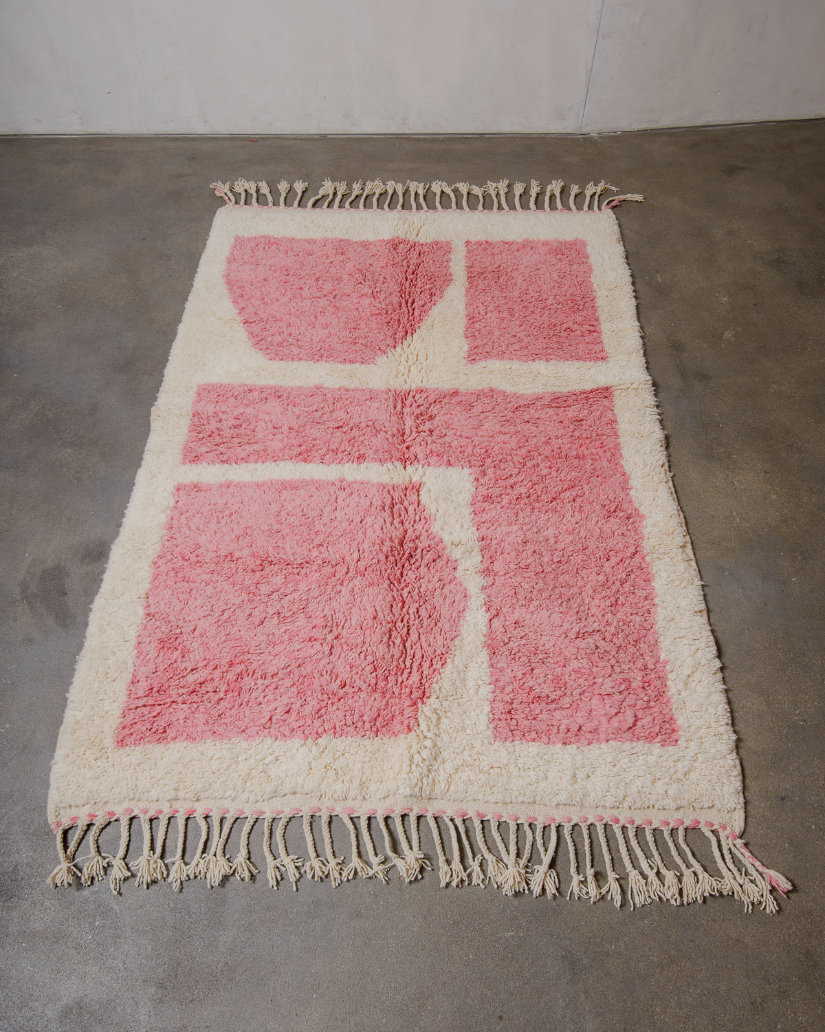 Pink and white wool Beniourain rug with fringes on concrete floor.
